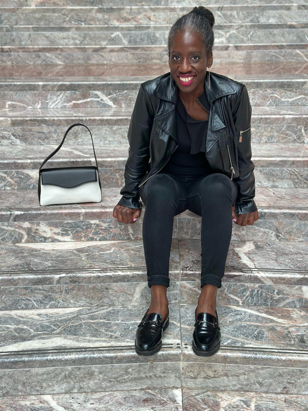 Finda sitting on steps next to a designer handbag.